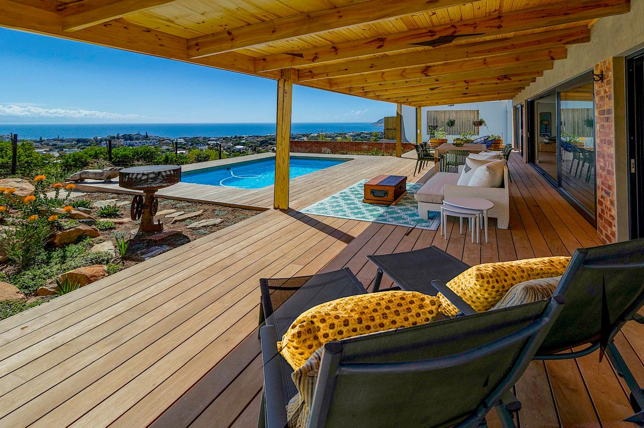 Covered deck lounge with yellow cushions overlooking pool and ocean